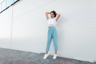 Sokakta vintage duvar yakınında poz beyaz spor ayakkabı şık bir dantel üst Kentsel sevimli genç kadın. Pretty trendy kız modeli bir yaz gününde şehirde rahatlatıcı sahiptir.