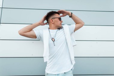 Modern bir binanın yakınında açık havada poz vintage güneş gözlüğü şık bir beyaz t-shirt şık saç modeli ile Genç kentsel hipster adam. Sevimli Amerikalı adam şehirde hafta sonu tadını çıkarıyor.