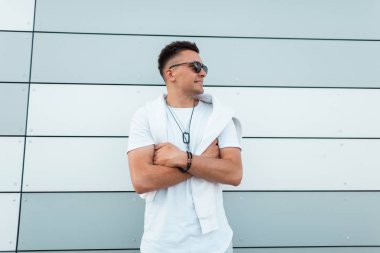 Modaya uygun beyaz bir t-shirt mavi moda kot güneş gözlüğü Genç mutlu Amerikalı adam hipster modern bir çizgili duvar yakınında şehirde poz olduğunu. Bir yaz gününde açık havada saç modeli ile Neşeli adam.