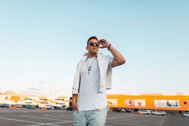 Vintage mavi kot bir moda beyaz t-shirt güneş gözlüğü genç Amerikan hipster adam bir yaz gününde şehirde açık havada poz veriyor. Çekici adam model park etti. Sokak stili.