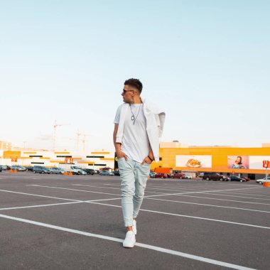 Spor ayakkabı bir trendy beyaz t-shirt kot moda güneş gözlüğü genç yakışıklı şık hipster adam şehirde yürüyor. Çekici adam modeli sokakta dinleniyor. Yaz stili.
