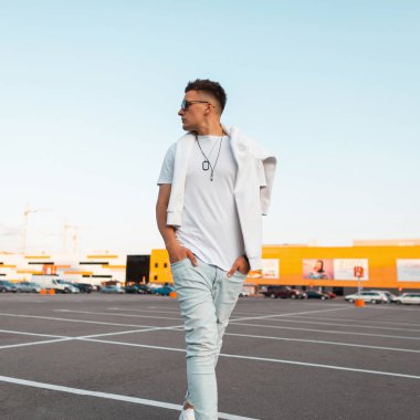 Şık bir saç modeli ile şık siyah güneş gözlüğü şık beyaz giysiler genç serin adam hipster bir şehir park parlak güneşli bir günde yürüyor. Yakışıklı Amerikalı erkek modeli. Yaz stili.