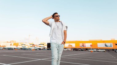 Modaya uygun siyah güneş gözlüğü ile modaya uygun siyah güneş gözlüğü moda beyaz yazlık giysiler modern serin genç adam bir şehir park parlak güneşli bir günde pozlar. Şehirli hipster. Sokak modası.