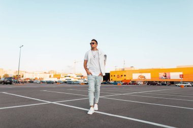 Spor ayakkabı şık bir beyaz t-shirt şık bir beyaz t-shirt güneş gözlüğü yakışıklı genç hipster adam açık bir yaz gününde şehir etrafında yürüyor. Sokakta dinlenmiş bir adam. Yaz sokak modası.