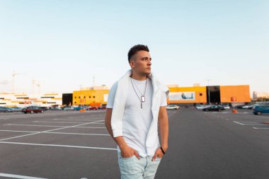 Modaya uygun mavi kot pantolonlu bir sweatshirt ile vintage beyaz bir t-shirt moda saç modeli ile çekici genç adam bir yaz gününde şehirde pozlar. Yakışıklı kentsel adam modeli açık havada.