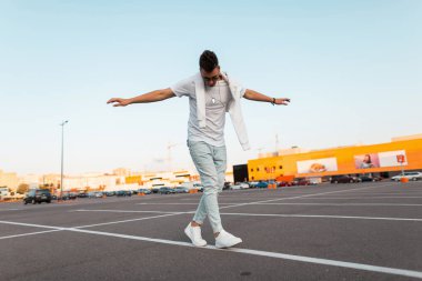 Genç Amerikalı adam hipster dengeyi korur ve asfalt üzerinde beyaz bir çizgi boyunca yürür. Vintage mavi kot moda spor ayakkabı güneş gözlüğü şık bir t-shirt çekici adam şehirde rahatlatır.