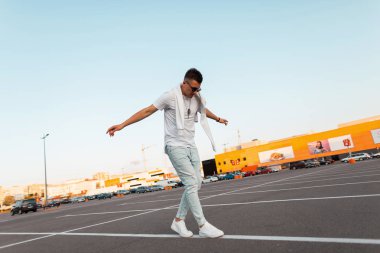 Güneş gözlüğü spor ayakkabı bir t-shirt modern genç adam yolda beyaz çizgi yürür ve dengesini korur. Çekici Amerikalı adam şehirde tatil tadını çıkarıyor. Aktif yaşam tarzı.