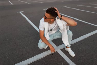 Spor ayakkabı şık bir beyaz t-shirt vintage mavi kot güneş gözlüğü Modern genç hipster adam yolda rahatlatır. Şehirde bir adam sokakta dinleniyor. Yaz gençlik moda. Moda erkek giyim.