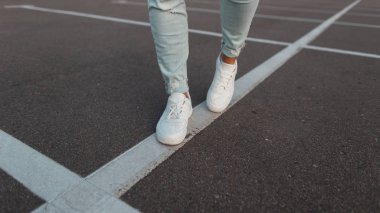Moda erkek beyaz deri beyaz spor ayakkabıları. Şık erkek ayakkabıları. Gündelik tasarım. Mavi kot pantolon ve moda ayakkabı erkek bacaklar Closeup. Yaz stili.