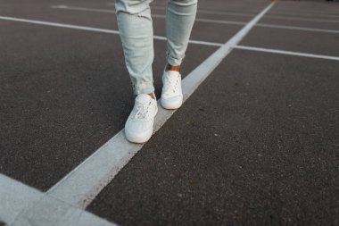 Moda yada mavi kot pantolongiymiş beyaz deri spor ayakkabılı modaya uygun genç adam. Şık erkek yazlık ayakkabılar. Gündelik tasarım. Erkek bacaklarının yakın çekim.