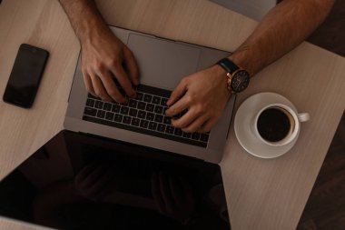 Modern bir dizüstü bilgisayarda çalışan iş adamı bir kafede bir masada oturuyor. Başarılı adam serbest klavyede yazıyor. Erkek ellerinin dizüstü bilgisayarla yakın çekimi. Masaüstünde en iyi görünüm.