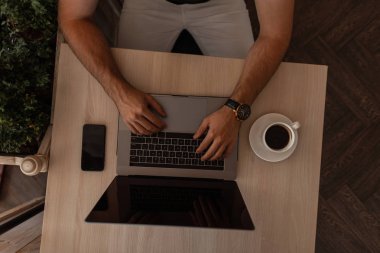 Bir kafede bir masada otururken modern bir dizüstü bilgisayar üzerinde çalışan freelancer adam. Başarılı adam yöneticisi klavyede yazıyor. Dizüstü bilgisayar ile erkek ellerinin yakın çekim. Masaüstünde en iyi görünüm.