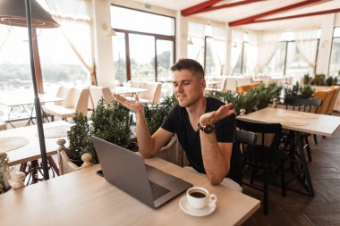 Genç mutlu işadamı modern bir dizüstü bilgisayar ile vintage bir kafede oturuyor ve yeni bir proje oluşturma başarı sevinir. Çekici pozitif freelancer uzaktan çalışır. Çalışma süresi.