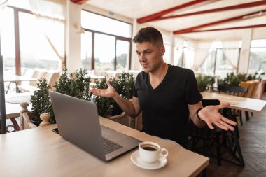 Siyah bir t-shirt çekici genç adam blogger bir kafede oturan bir dizüstü bilgisayar bakar ve sürpriz ifade eder. Yakışıklı adam yöneticisi yeni bir proje üzerinde kapalı çalışıyor.