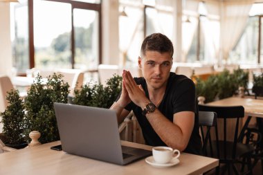 Başarılı yakışıklı genç freelancer bir kafede kahve bir fincan için yeni bir mali proje ile internette bir dizüstü bilgisayar üzerinde çalışıyor. İş adamı ofiste uzaktan çalışıyor.