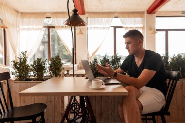Başarılı genç adam pencerelere yakın bir ofiste bir masada oturur ve bir fincan kahve üzerinde bir öğle yemeği molası bir dizüstü bilgisayar üzerinde çalışır. Freelancer iş adam uzaktan internet üzerinde yeni bir proje üzerinde çalışıyor.