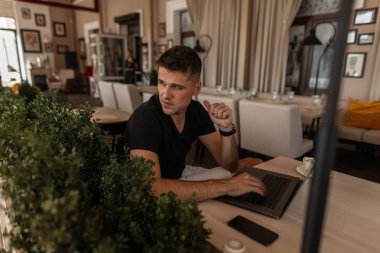 Şık bir t-shirt çekici genç yönetici adam bir vintage kafede bir masada oturan bir klavye üzerinde yazıyor. Yakışıklı iş adamı internet üzerinde bir dizüstü bilgisayar üzerinde uzaktan çalışıyor. Çalışma süresi.