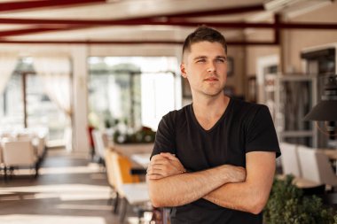 Güneşli bir yaz gününde vintage kafede ayakta poz şık bir siyah t-shirt şık bir saç modeli ile genç bir adam Modern Amerikan erkek modeli. Nice kentsel adam bir restoranda dinlenmek sahiptir.