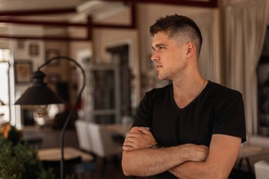 Şık saç modeli ile şık genç adam uzakta kapalı görünüyor. Vintage iç bir kafede poz şık bir siyah t-shirt çekici işadamı adam.