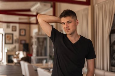 Şehirde bir vintage kafede ayakta poz şık bir siyah t-shirt şirin bir gülümseme ile şık bir saç modeli ile genç yakışıklı adam. Avrupa modern erkek modeli kapalı.