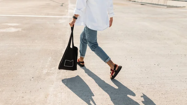 Jonge man in modieuze zomer kleren in stijlvolle rode sandalen met een zwarte Vintage tas loopt langs de straat. Close-up mannelijke benen. Trendy herenkleding. Stijlvolle look. — Stockfoto