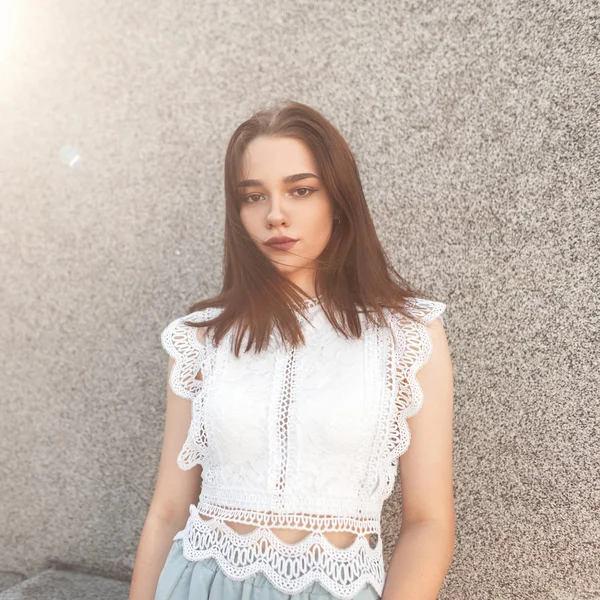 Portrait of an attractive young woman with natural make-up in an elegant lace white blouse on a background gray wall on a bright sunny day. Pretty girl model enjoys the sunshine outdoors. Summer style — Stock Photo, Image