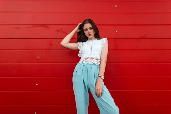Schattige jonge Europese vrouw in een elegante Lace shirt in blauwe broek met bruin haar staat in de stad in de buurt van een vintage rode houten muur. Stijlvolle moderne meisje. Modieuze zomerlook. — Stockfoto