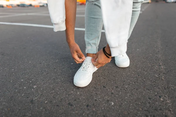 Stylish Young Man staat op de stoep en het binden van schoenveters op leren witte sneakers op een zomerdag. Mannen benen close-up. Nieuwe seizoenscollectie modieuze heren schoenen. — Stockfoto