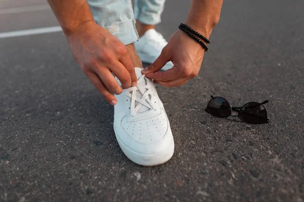 Männerhände richten Schnürsenkel auf weißen modischen Lederturnschuhen. neue Kollektion stilvoller Herrenschuhe und Accessoires. Nahaufnahme. — Stockfoto