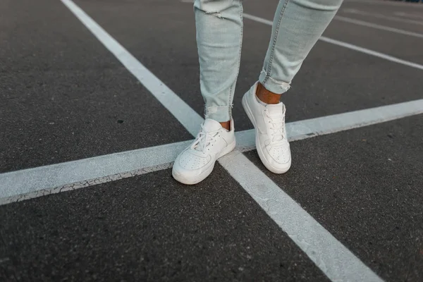 Mannelijke benen close-up. Jonge stijlvolle man in leren witte schoenen staat op de weg op een zomerdag. Nieuwe seizoensgebonden collectie van modieuze heren sneakers. — Stockfoto