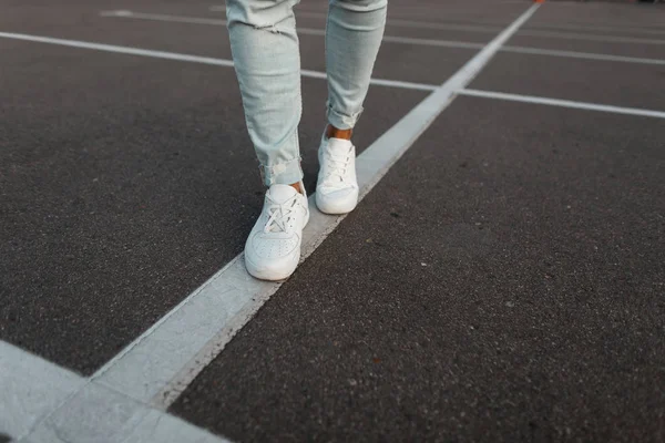 Trendiger junger Mann in weißen Lederturnschuhen in modischer blauer Jeanshose. stylische Sommerschuhe für Männer. Casual Design. Nahaufnahme männlicher Beine. — Stockfoto