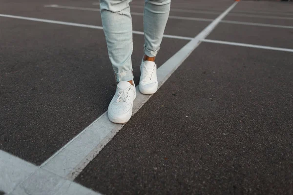 Moda yada mavi kot pantolongiymiş beyaz deri spor ayakkabılı modaya uygun genç adam. Şık erkek yazlık ayakkabılar. Gündelik tasarım. Erkek bacaklarının yakın çekim.