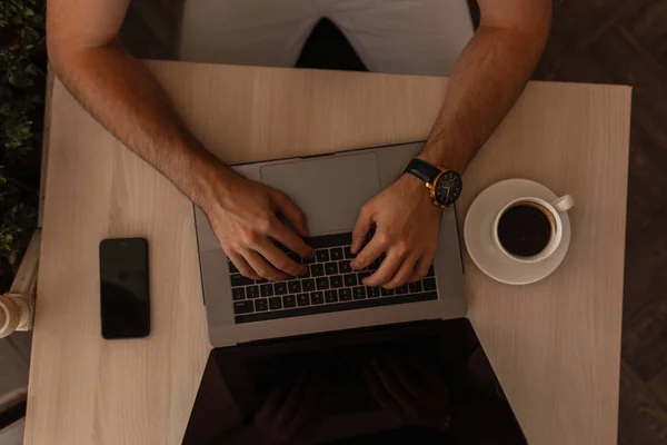 Blogger obchodník pracuje na moderním laptopu v kanceláři. Horní pohled na dřevěnou plochu s laptopem s šálkem kávy a telefonem. Close-up. Vzdálená práce. — Stock fotografie