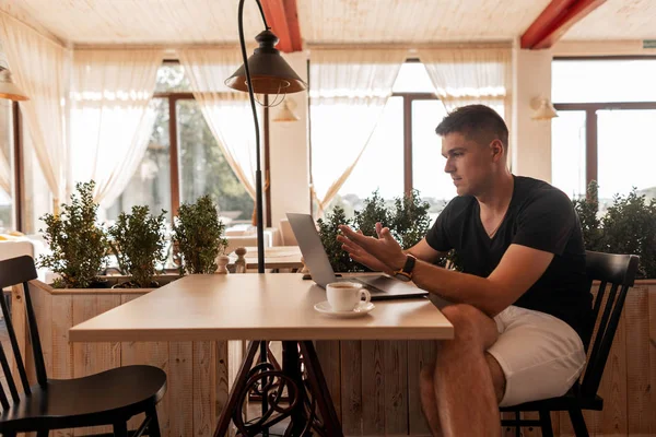 Başarılı genç adam pencerelere yakın bir ofiste bir masada oturur ve bir fincan kahve üzerinde bir öğle yemeği molası bir dizüstü bilgisayar üzerinde çalışır. Freelancer iş adam uzaktan internet üzerinde yeni bir proje üzerinde çalışıyor.