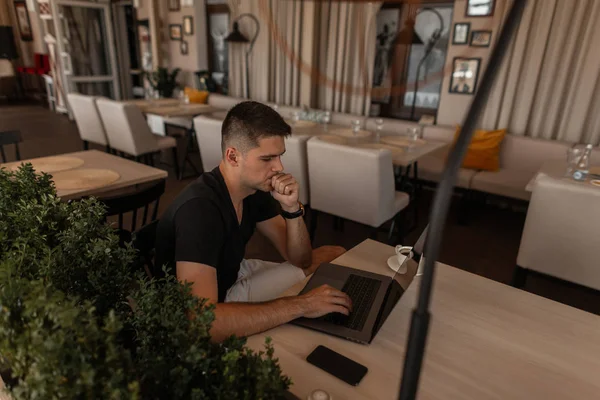 Profesyonel genç tasarımcı adam kapalı yeni bir yaratıcı proje ile Internet üzerinde bir dizüstü bilgisayar üzerinde çalışır. Şık serbest adam bir vintage kafede otururken bir klavye üzerinde yazıyor. Uzaktan çalışma. 