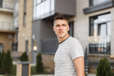 Şık bir saç modeli ile şık bir çizgili t-shirt Çekici genç adam modern bir binanın yakınında şehirde bir sokakta seyahat. Kentsel yakışıklı adam modeli bir yürüyüş sahiptir. Yaz modası.