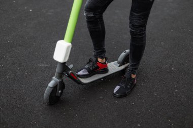 Bir yaz gününde bir elektrikli scooter trendy siyah spor ayakkabı siyah kot şık erkek bacaklar. Moda adam modern bir scooter yakınında bir asfalt üzerinde duruyor. Close.