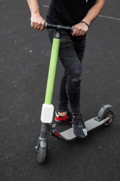 Nahaufnahme des männlichen Körpers in stilvoller Kleidung und Elektroroller. Sportlicher Typ fährt auf einem modernen Roller auf einem Basketballplatz. Aktivurlaub. — Stockfoto