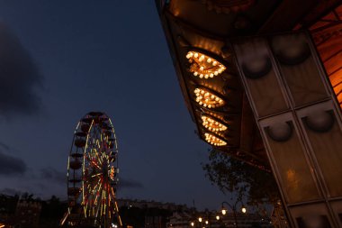 Gece mavi gökyüzünün arka planında lunapark. Parlak ışıklar ve sarı ampuller ile bir atlıkarınca parçası ile bir vintage dönme dolap bir bakış. Aile ile hafta sonu.
