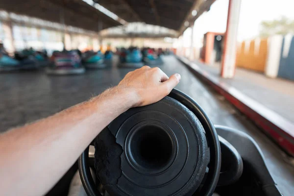 El joven disfruta montando en un coche de parachoques eléctrico en un autódromo en un parque de atracciones. Primer plano de la mano masculina en el volante de un coche. Vacaciones . — Foto de Stock