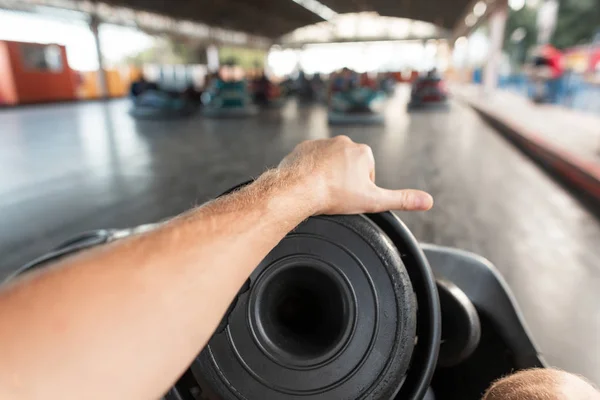 Closeup of a male hand with a black electric car steering wheel. The guy rides a bumper car on the autodrome. Weekend in the amusement park. — Stock Photo, Image