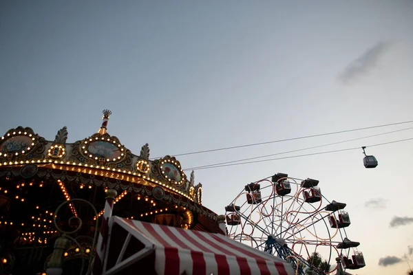 Vergnügungspark mit einem Oldtimer-Karussell mit Lichtern und einem Riesenrad mit bunten Ständen am Abend. Freizeitpark in Europa. Urlaub — Stockfoto