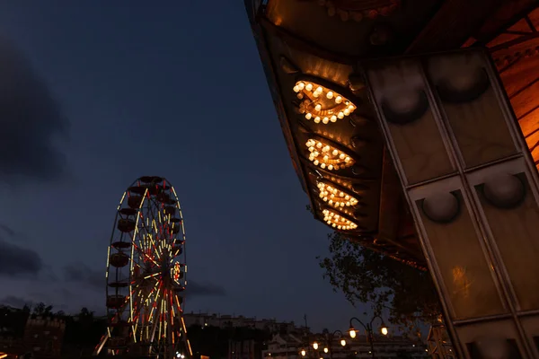 Vergnügungspark am Abend vor blauem Himmel. Ein Blick auf ein historisches Riesenrad mit hellen Lichtern und ein Karussell mit gelben Glühbirnen. Wochenende mit der Familie. — Stockfoto