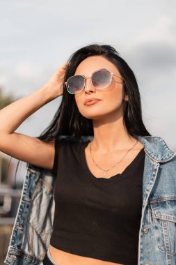 Siyah ceketli, şık siyah gözlüklü oldukça çekici genç hippi kadın klasik ahşap bir duvarın yanında rahatlıyor. Moda elbiseli seksi esmer kız model dışarıda dinleniyor..