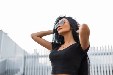 Şık siyah saçlı, şık siyah tişörtlü, şık, siyah güneş gözlüklü, şehirde poz veren güzel bir manken. Sokaktaki seksi hippi kız hafta sonunun tadını çıkarıyor..
