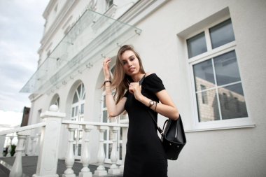 Hoş bir gülümsemesi olan, siyah, zarif bir elbisesi ve çıplak omuzları olan, deri renkli, şık bir sırt çantası olan çekici genç bir kadın şehirde dolaşmaktan zevk alıyor. Modern şehir kızı cadde boyunca yürüyor..