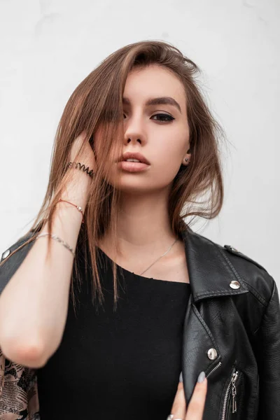 Retrato de uma jovem bonita na moda com belos olhos com lábios sexy com maquiagem natural em roupas pretas na moda em um fundo de uma parede branca ao ar livre. Menina bonita atraente posando . — Fotografia de Stock