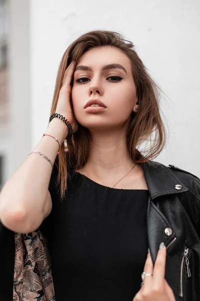 Portrait of a female face with beautiful natural makeup with sexy lips. Attractive pretty sensual girl model in stylish black clothes posing near a white building on a autumn day. — Stock Photo, Image