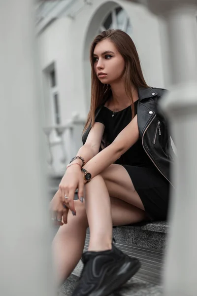 Junge Europäerin in stylischer schwarzer Kleidung in trendigen Schuhen sitzt auf einer Steintreppe in der Stadt. modische Mädchen Modell ruht in einem Herbsttag im Freien. lässige Jugendkleidung für Frauen. — Stockfoto