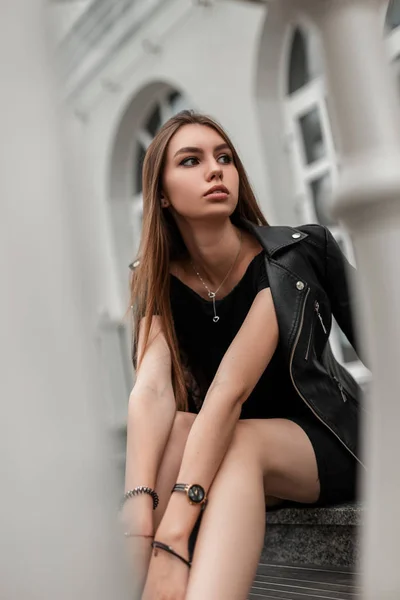 Jovem mulher elegante em roupas pretas elegantes senta-se nos degraus da cidade perto de um edifício branco. Linda moda menina modelo de moda ao ar livre. Roupas de mulher na moda. Outono look casual . — Fotografia de Stock